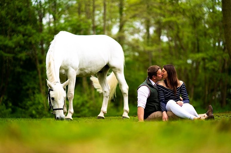couple kissing on their pre-wedding photoshoot on the grass next to a horse