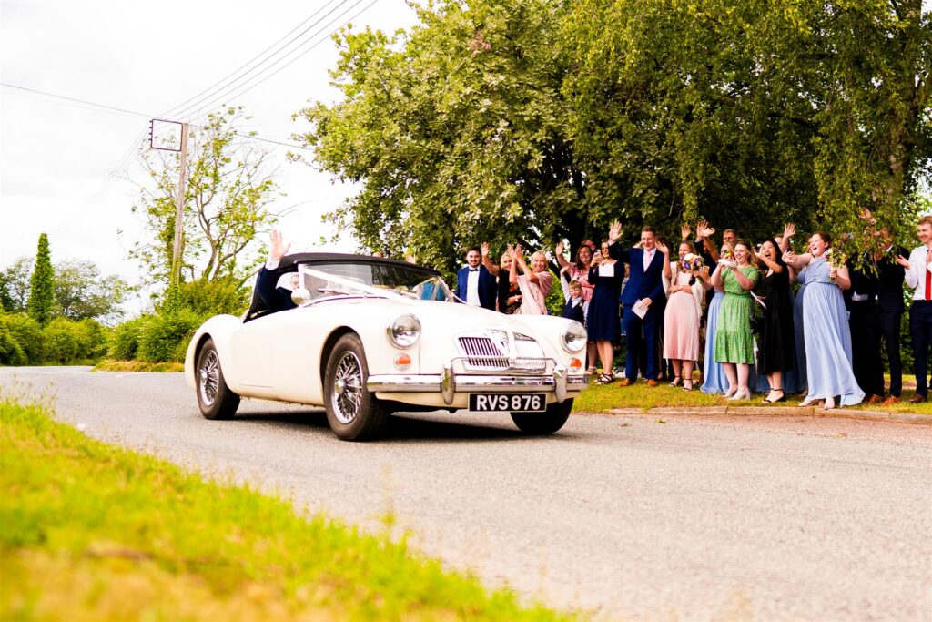 bride and groom driving off in old school car on their wedding day in Suffolk